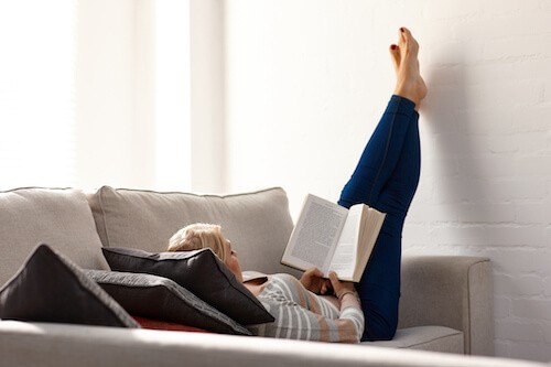 woman elevates legs while reading book to reduce leg swelling